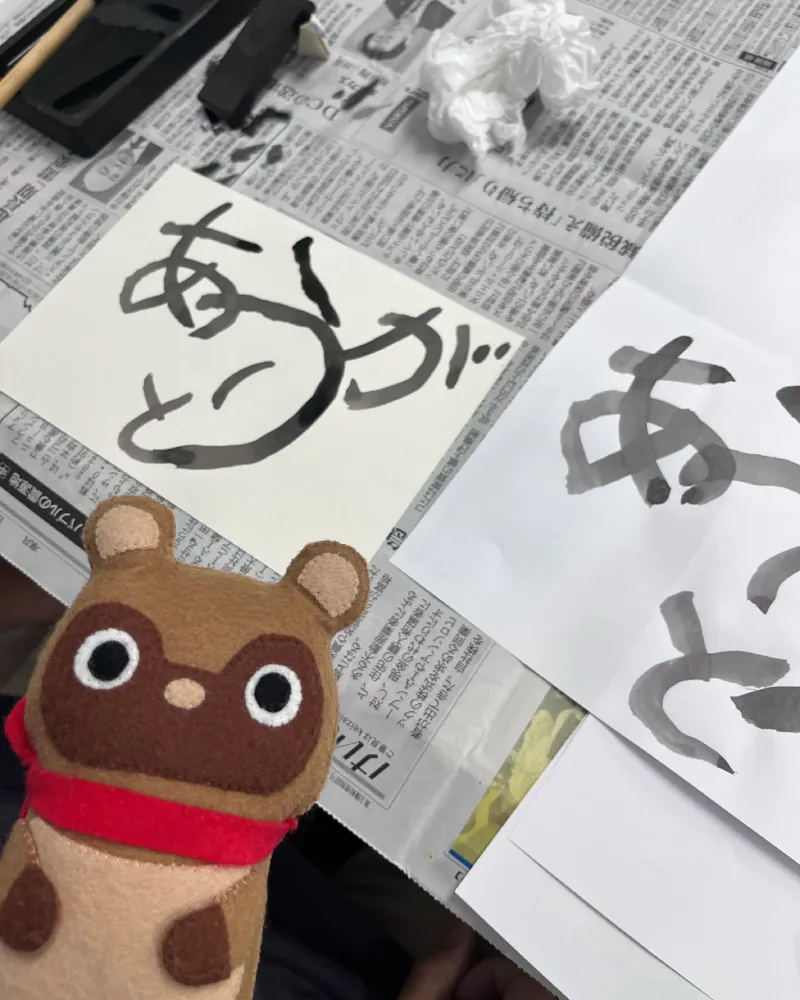 和游字体験で練習中の『ありがとう』の筆文字と、見守るマスコットキャラクターのたぬきち