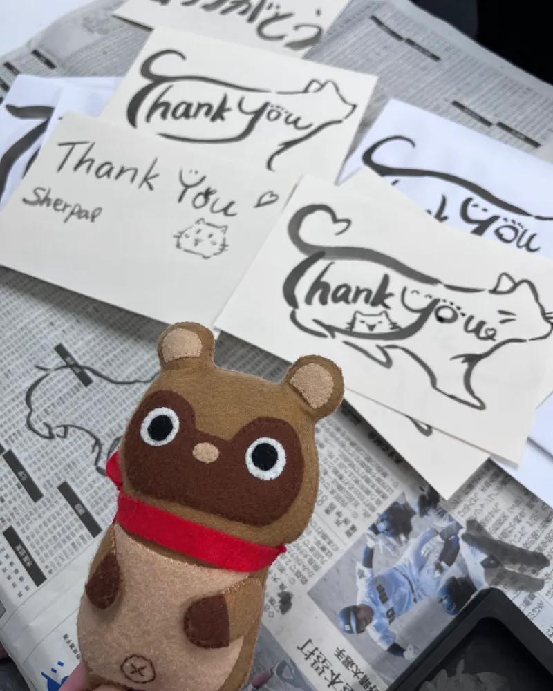 猫のイラストと『Thank You』の文字を組み合わせた筆文字カードと、手前に並ぶマスコットキャラクターのたぬきち
